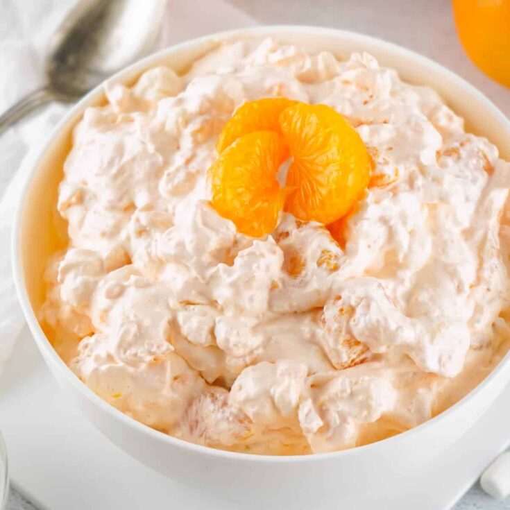 a white bowl on a white plate filled with a orange fluff jello salad