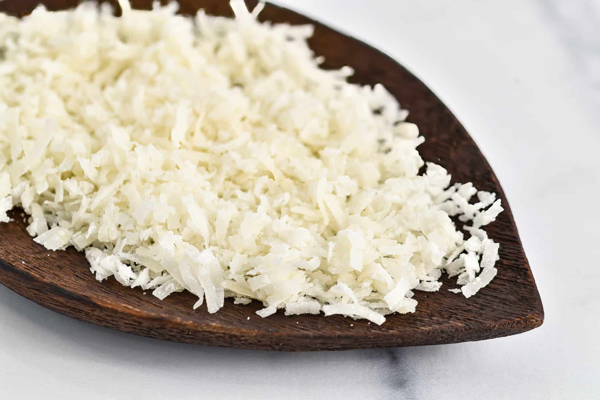 Fresh shredded sweetened coconut flakes scattered in the center of a wooden leaf platter on a marble counter