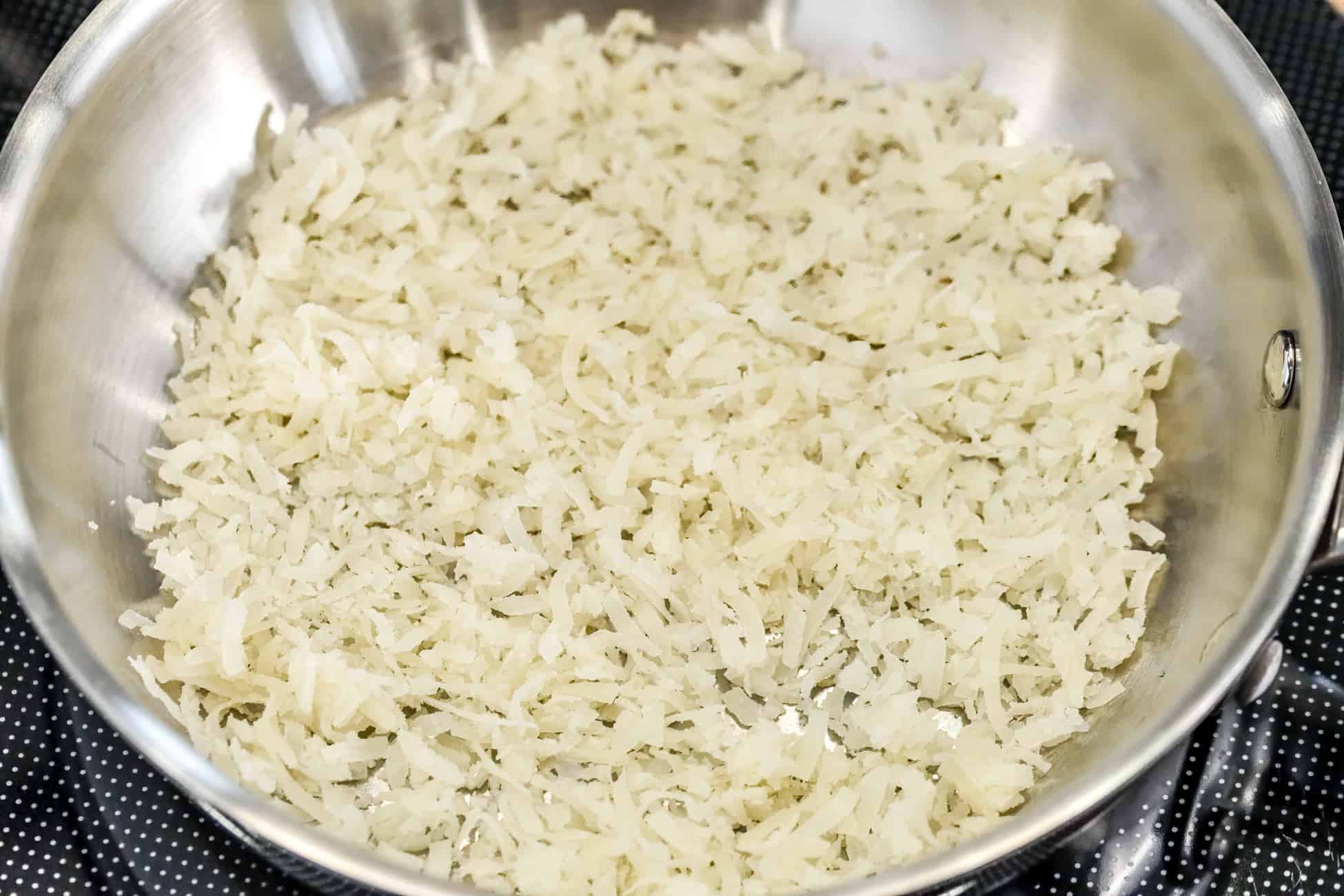 Shredded coconut in a stainless steel skillet on a stovetop