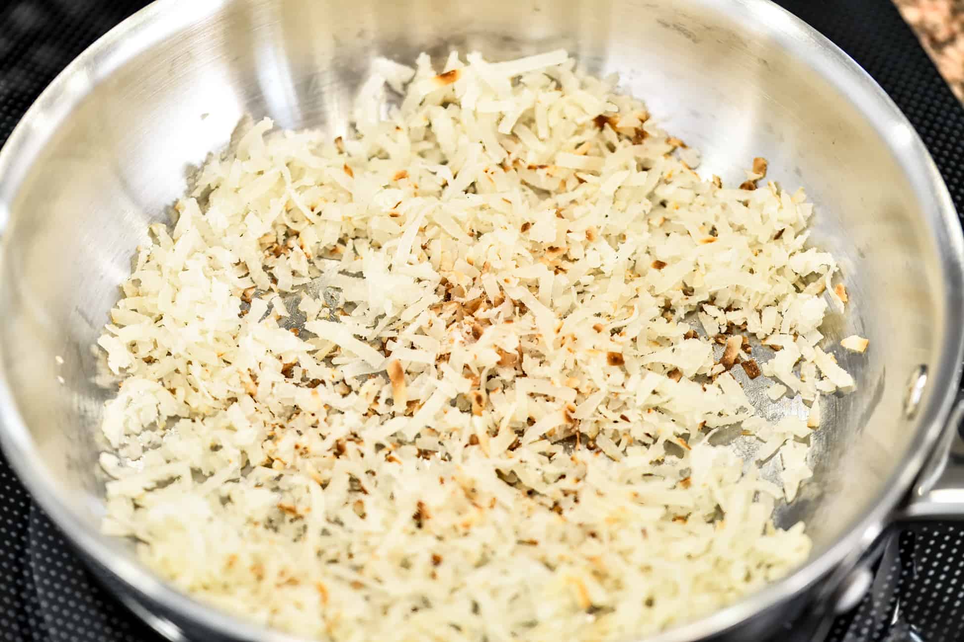 toasted coconut flakes in a stainless steel pan on a stove top