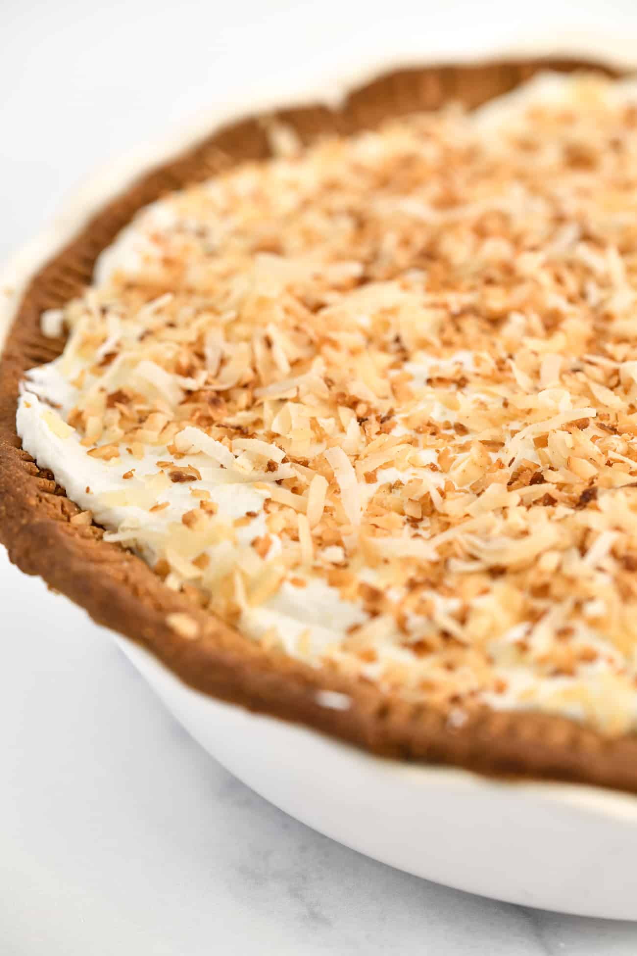 Close up view of the top of a coconut cream pie with toasted coconut flakes sprinkled on the top