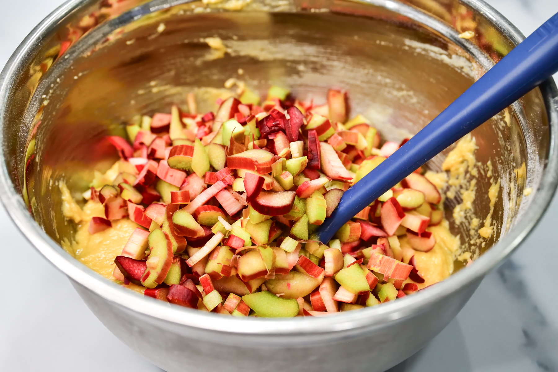 Diced Rhubarb poured on top of the muffin batter in a silver mixing bowl