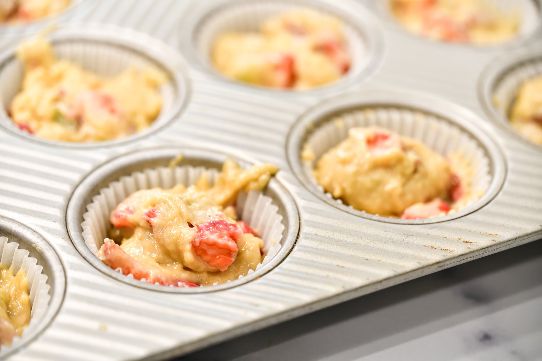 muffin batter in a silver muffin tray filling about 3/4 full with white paper liner