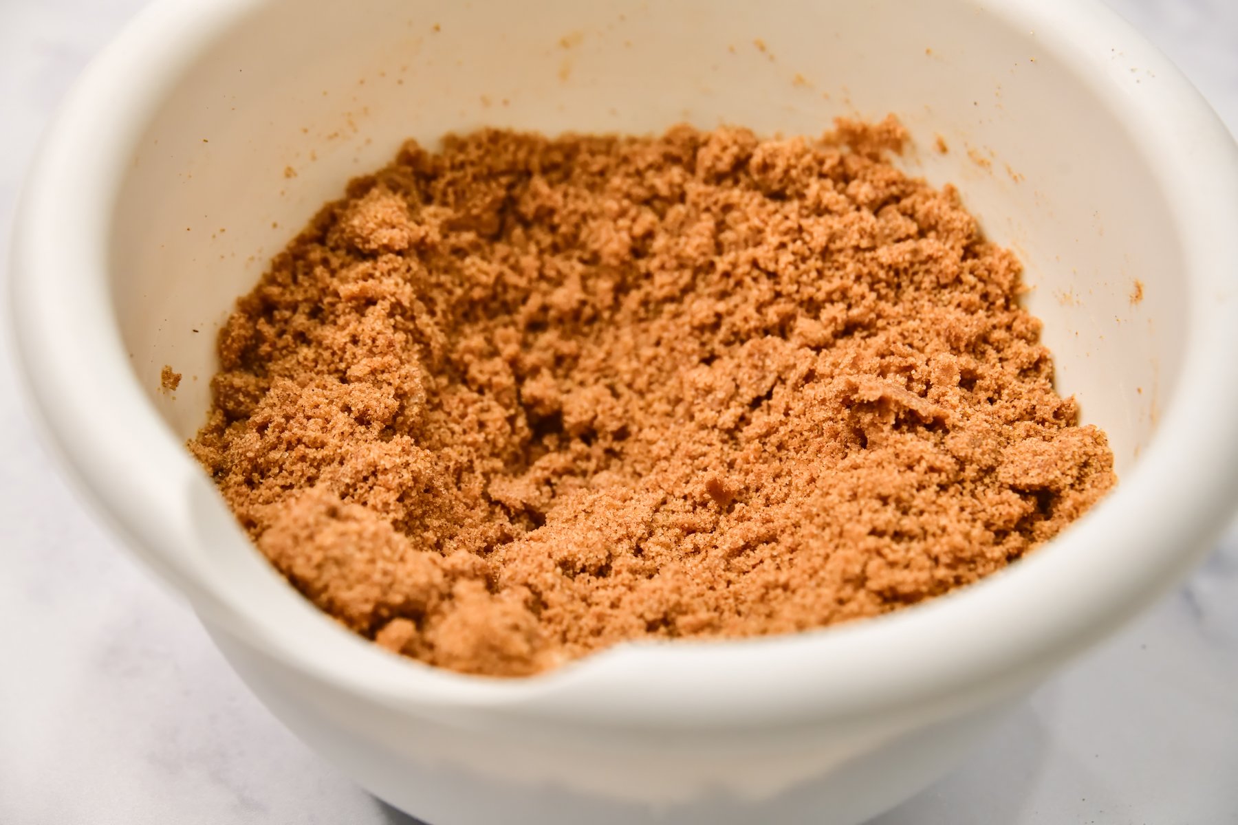 Homemade cinnamon streusel in a white mixing bowl on a marble surface