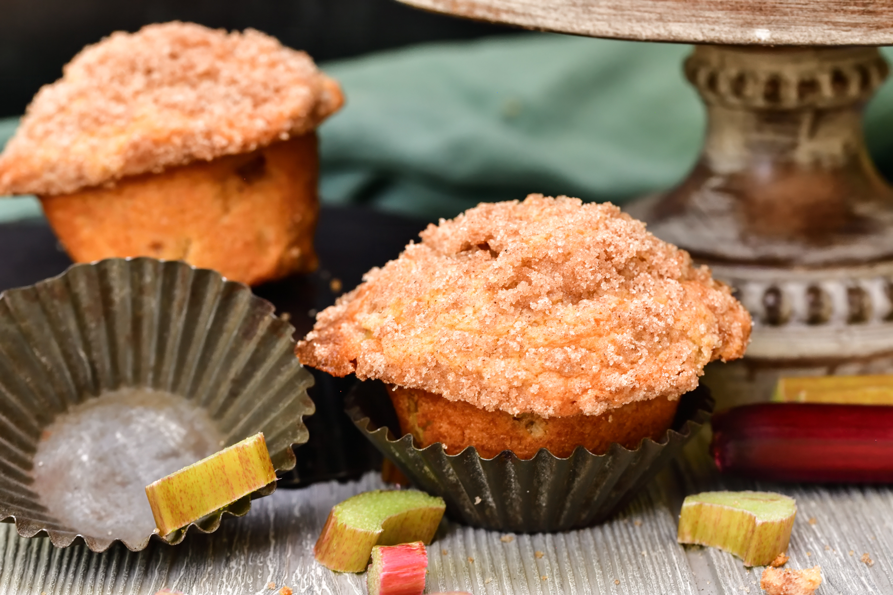 twoo rhubarb muffins next to old fashioned tin muffin liners and fresh chopped rhubarb on a wooden surface