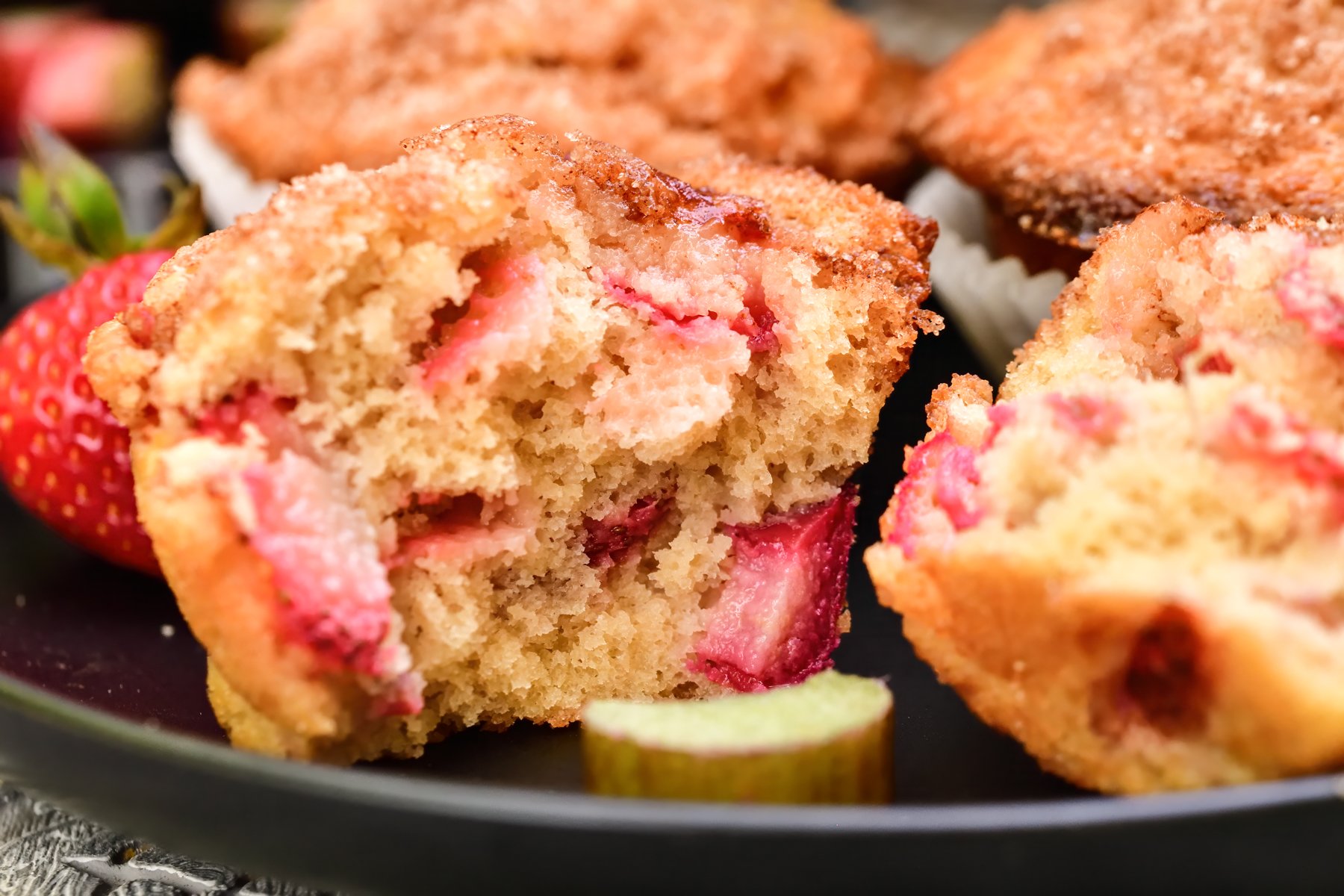 Single muffin on a black plate torn apart displaying chunks of strawberries and rhubarb inside