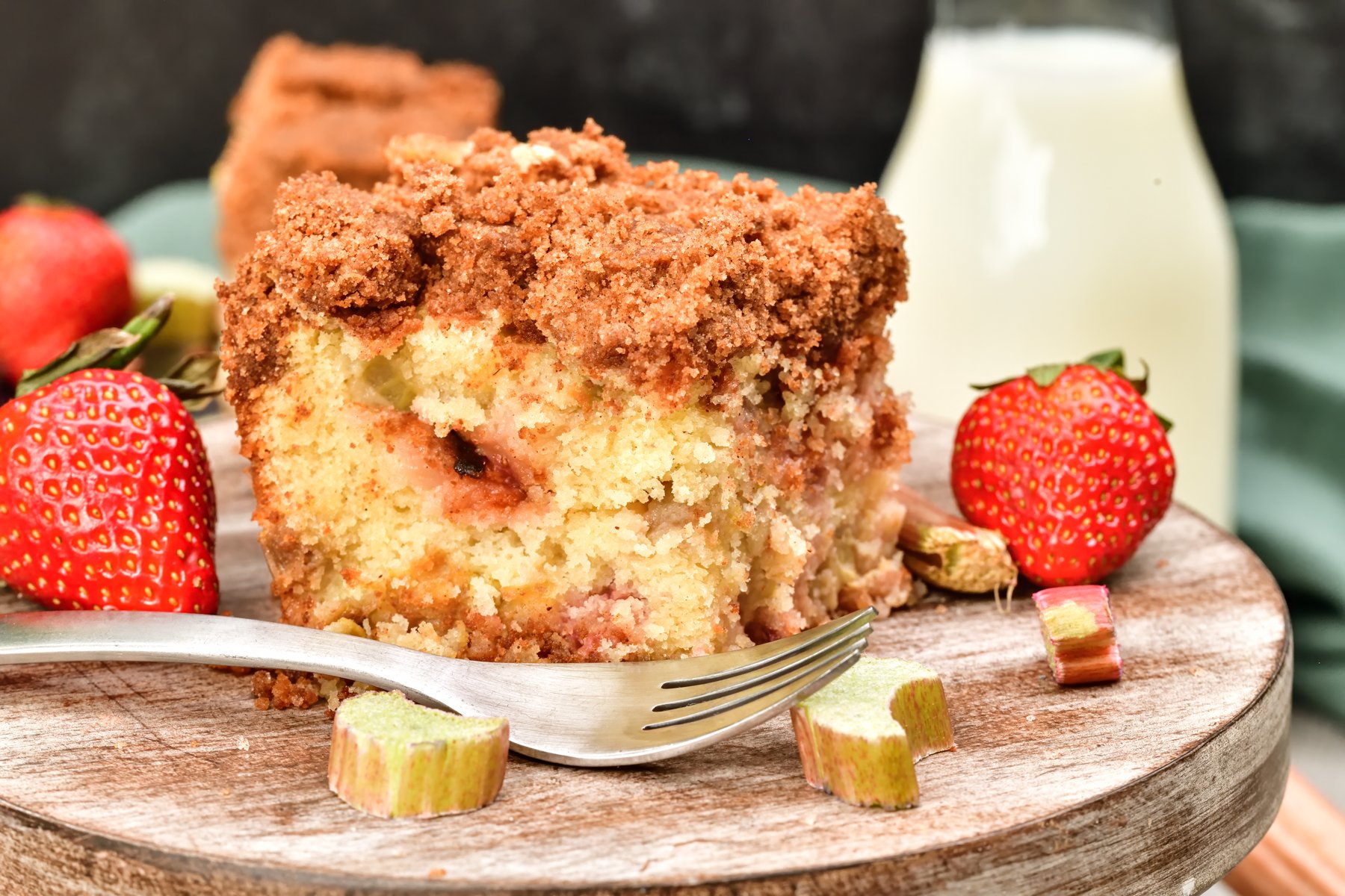 Side view of a rhubarb coffee cake on a wood cake stand with strawberries and rhubarb
